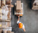 Warehouse worker transporting packaged boxes on a pallet jack in a wholesale distribution warehouse.